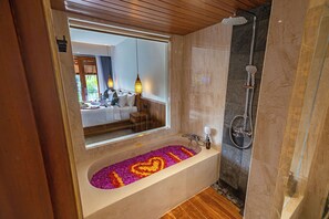 A bathroom with a large bathtub, a shower, and a mirror reflecting a bedroom. - The Dura Ubud (Ubud)