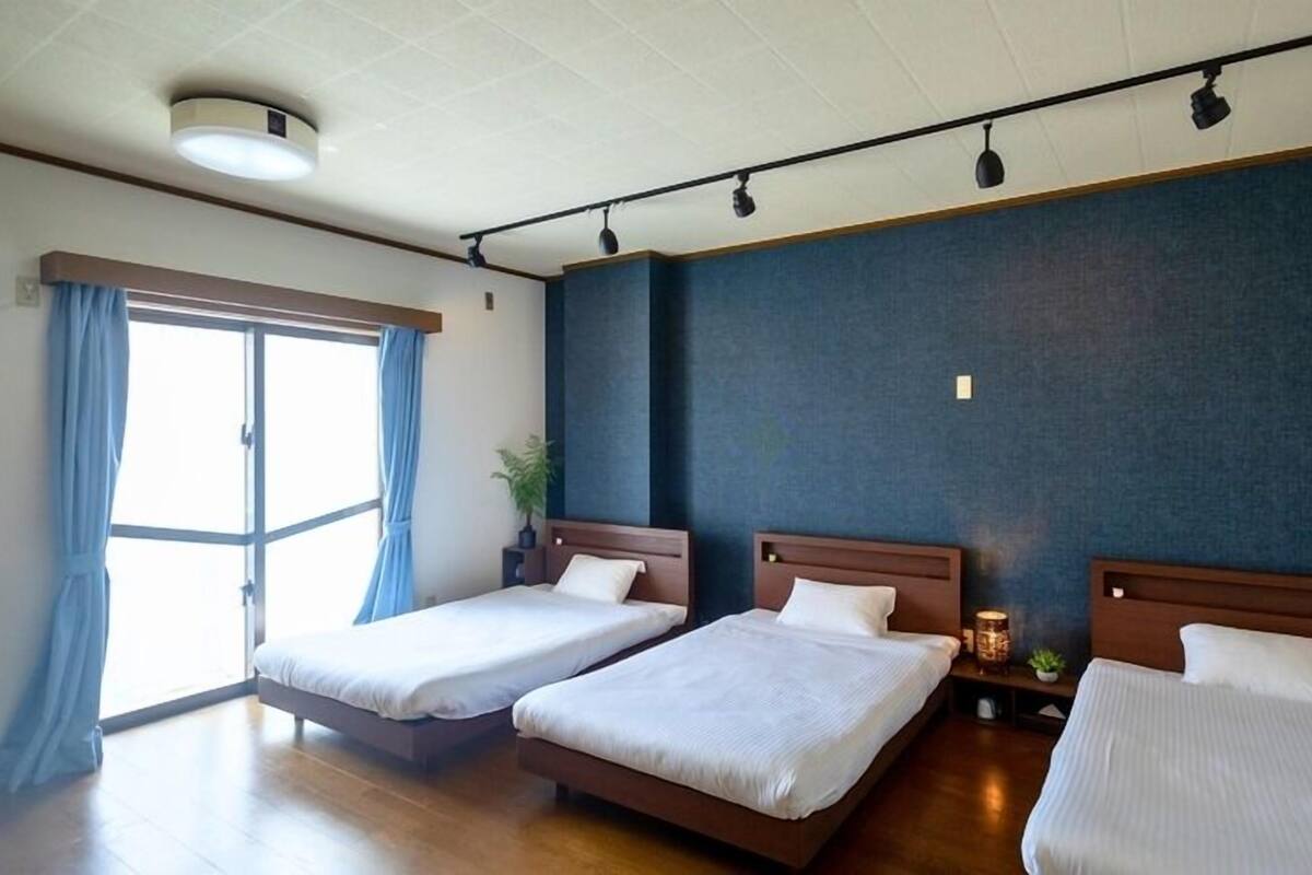 Habitación de hotel con dos camas, un ventanal con cortinas, una lámpara de techo y una lámpara de pared.