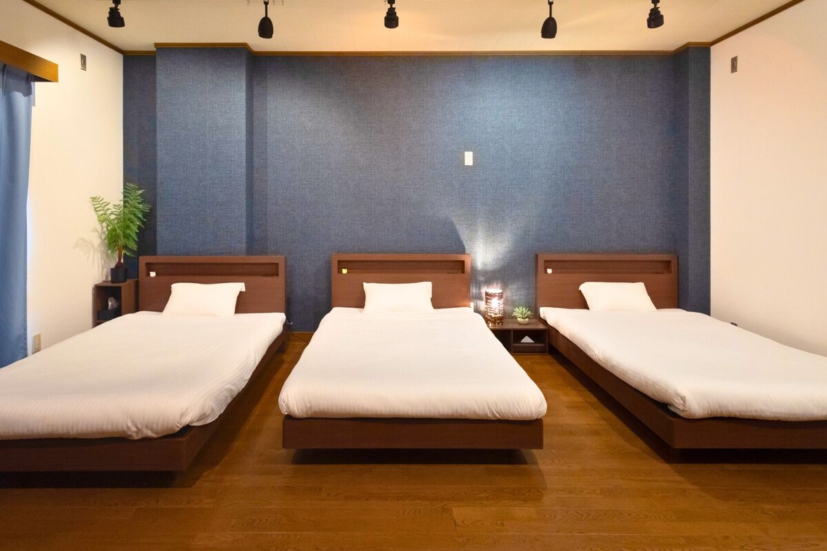 Ein Hotelzimmer mit drei Einzelbetten, Holz-Kopfteilen und einer blauen Wand.