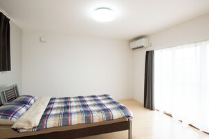 Una habitación con una cama, una lámpara en el techo, un equipo de aire acondicionado y una ventana con cortinas.