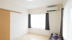 A room with a wooden wardrobe, a window with curtains, an air conditioning unit, and a bed with a plaid blanket. - Destiny Seaside Village (Sakaiminato)