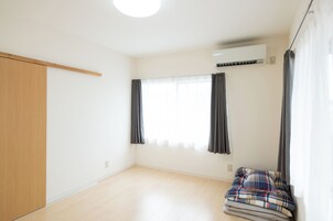 Una habitación con un armario de madera, una ventana con cortinas, un equipo de aire acondicionado y una cama con una manta escocesa.