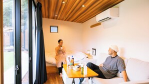 A room with a bed, a table with toiletries, a white couch, and an air conditioning unit.