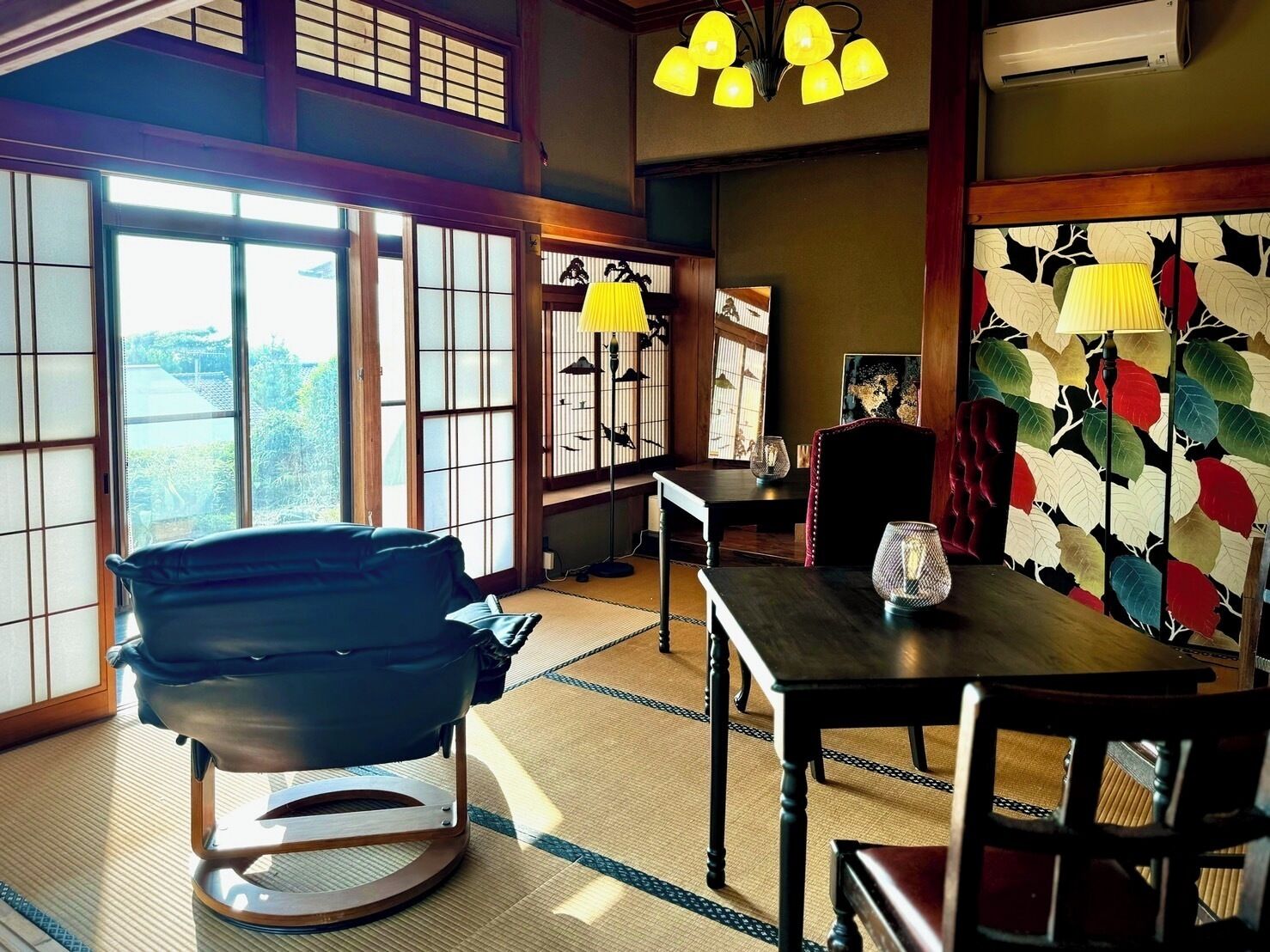 A traditional Japanese room with tatami flooring, a low table, a chair, and a decorative wall with a leaf pattern.