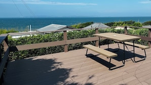 Una terraza de madera con una mesa de picnic y barandilla con vista al océano.