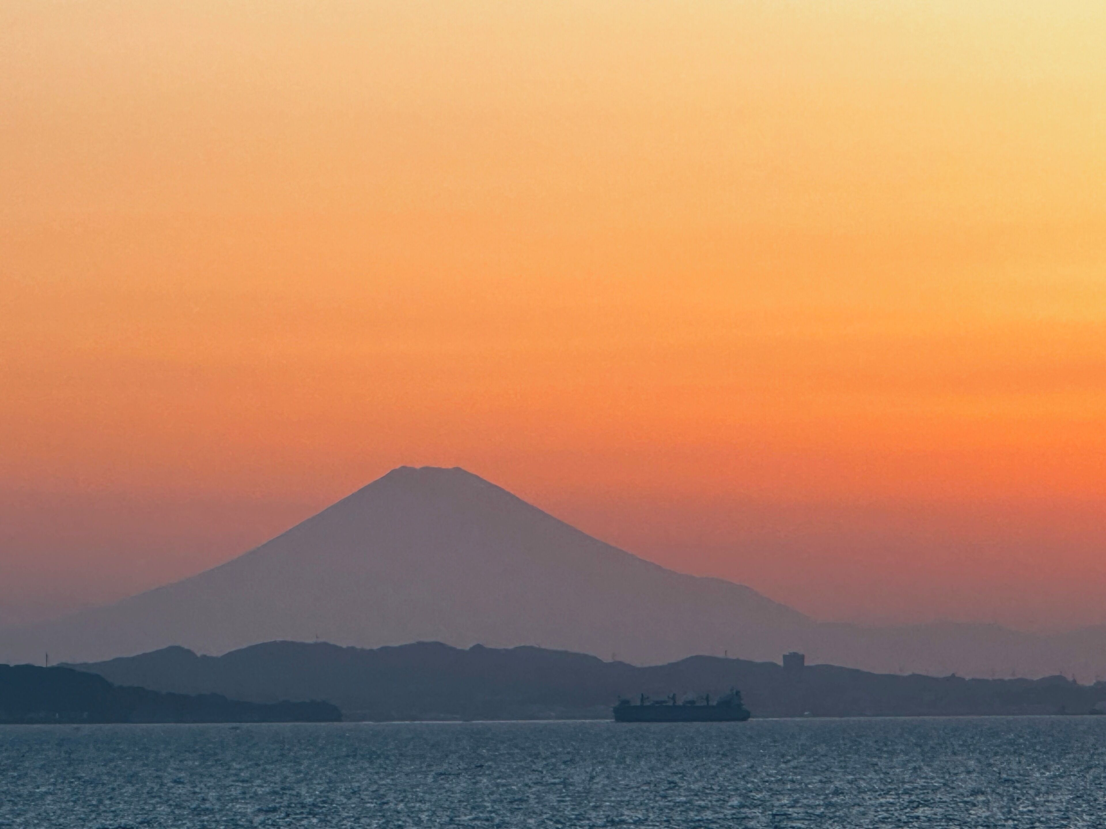 A mountain silhouette against a sunset sky, a body of water, and a distant ship.