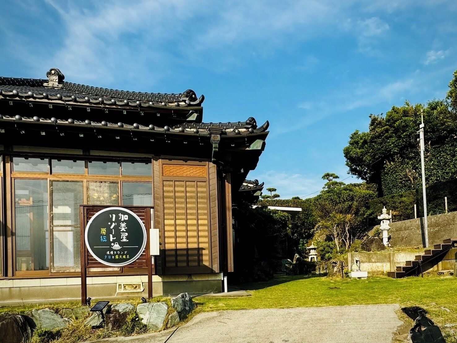 Un edificio japonés tradicional con un letrero, un farol de piedra y una pequeña pagoda al fondo.