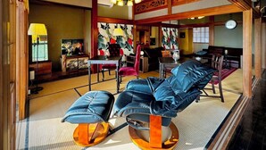 Una habitación tradicional japonesa con suelo de tatami, una mesa baja con cojín, un sofá con cojines y una lámpara colgante.
