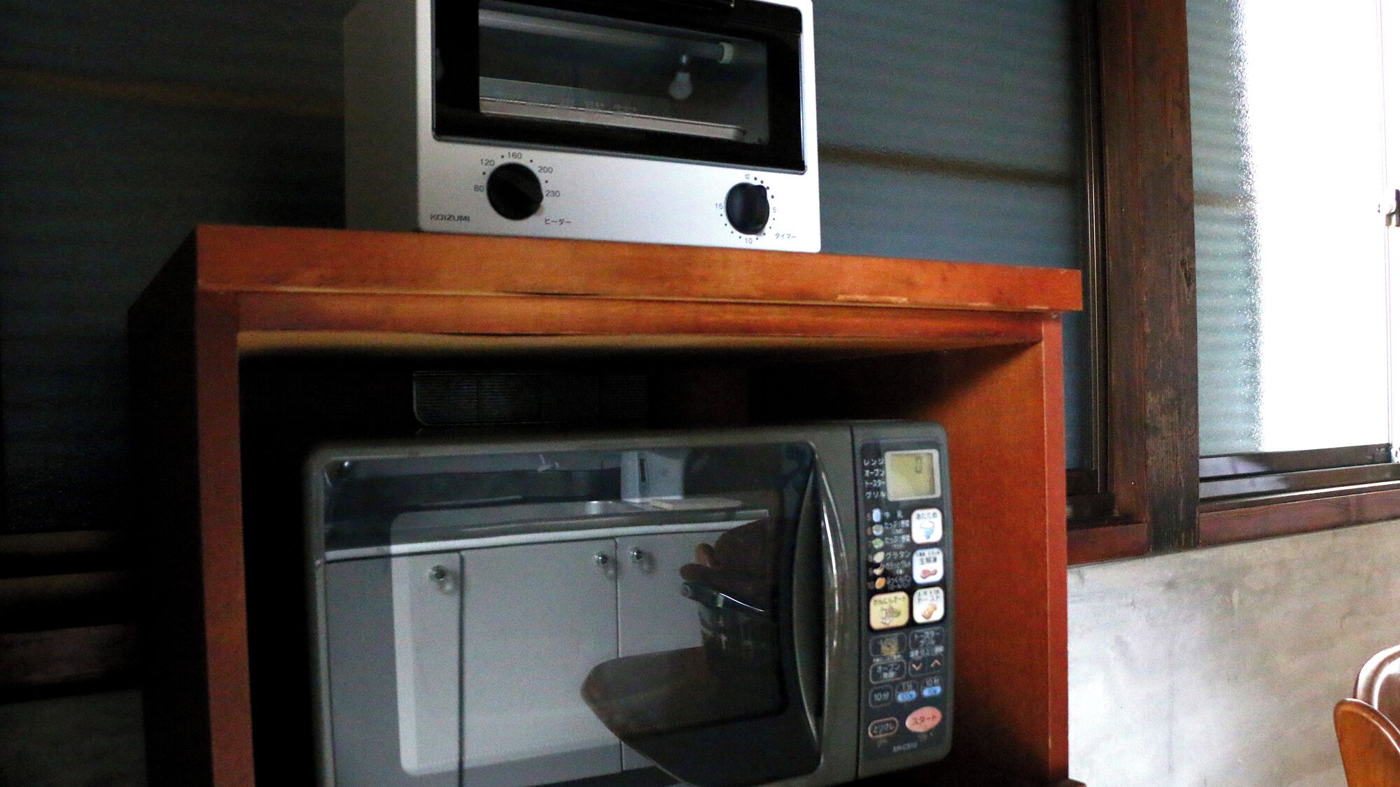 A microwave oven with a digital display and control panel, placed on a wooden shelf.
