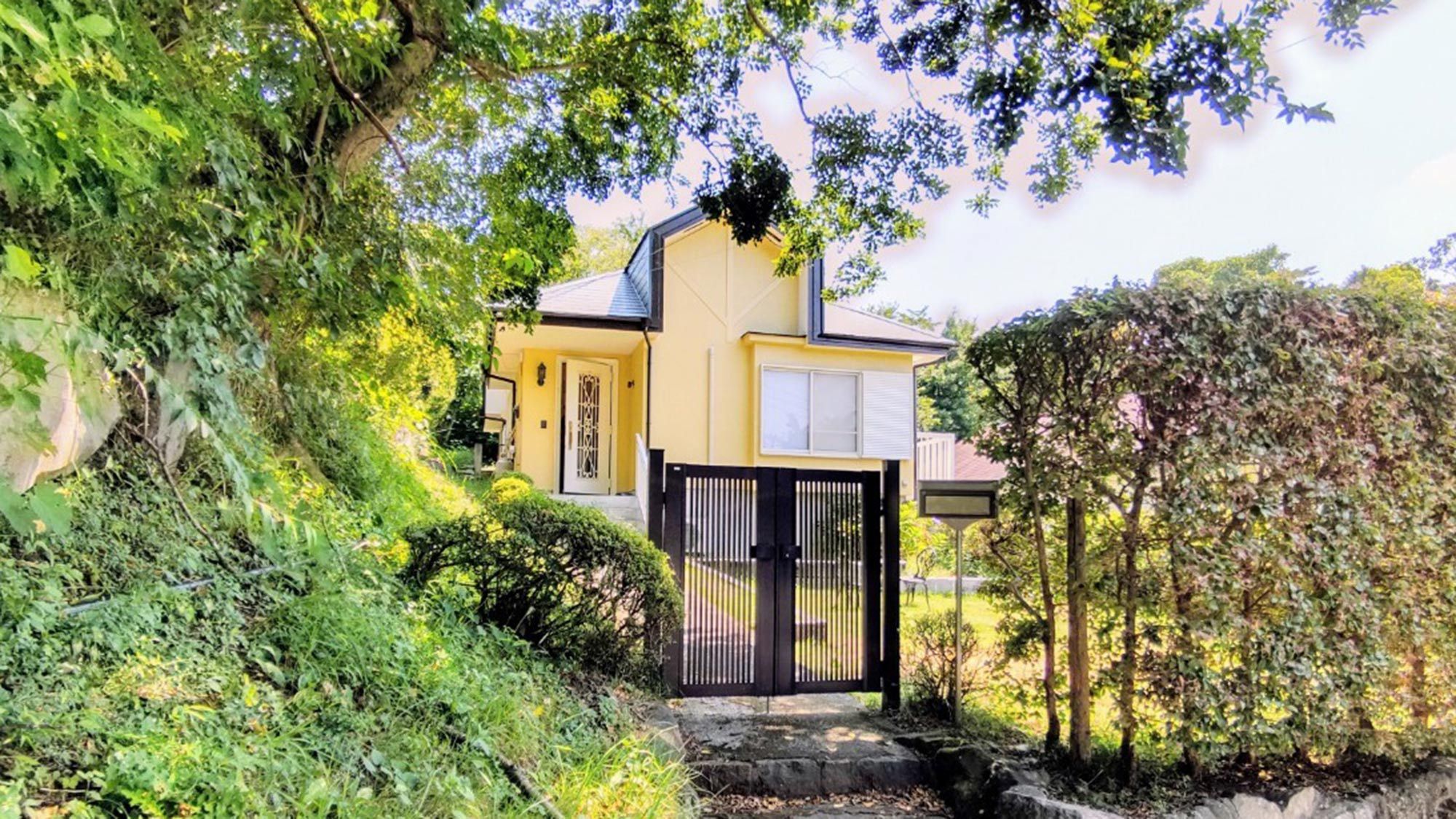 A house with a black gate, surrounded by lush greenery and trees.