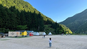 A beach with tents and a small building, surrounded by forested hills.