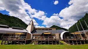 Un edificio tradicional japonés con un tejado empinado, rodeado de exuberante vegetación y montañas.