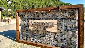 A wooden sign with the text "OCHIDANI CAMP" mounted on a stone wall.