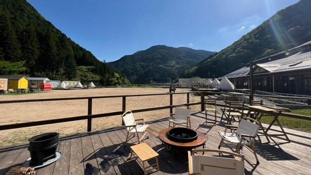 A wooden deck with outdoor seating, a fire pit, and a view of a beach and mountains.