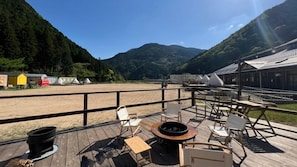 A wooden deck with outdoor seating, a fire pit, and a view of a beach and mountains.