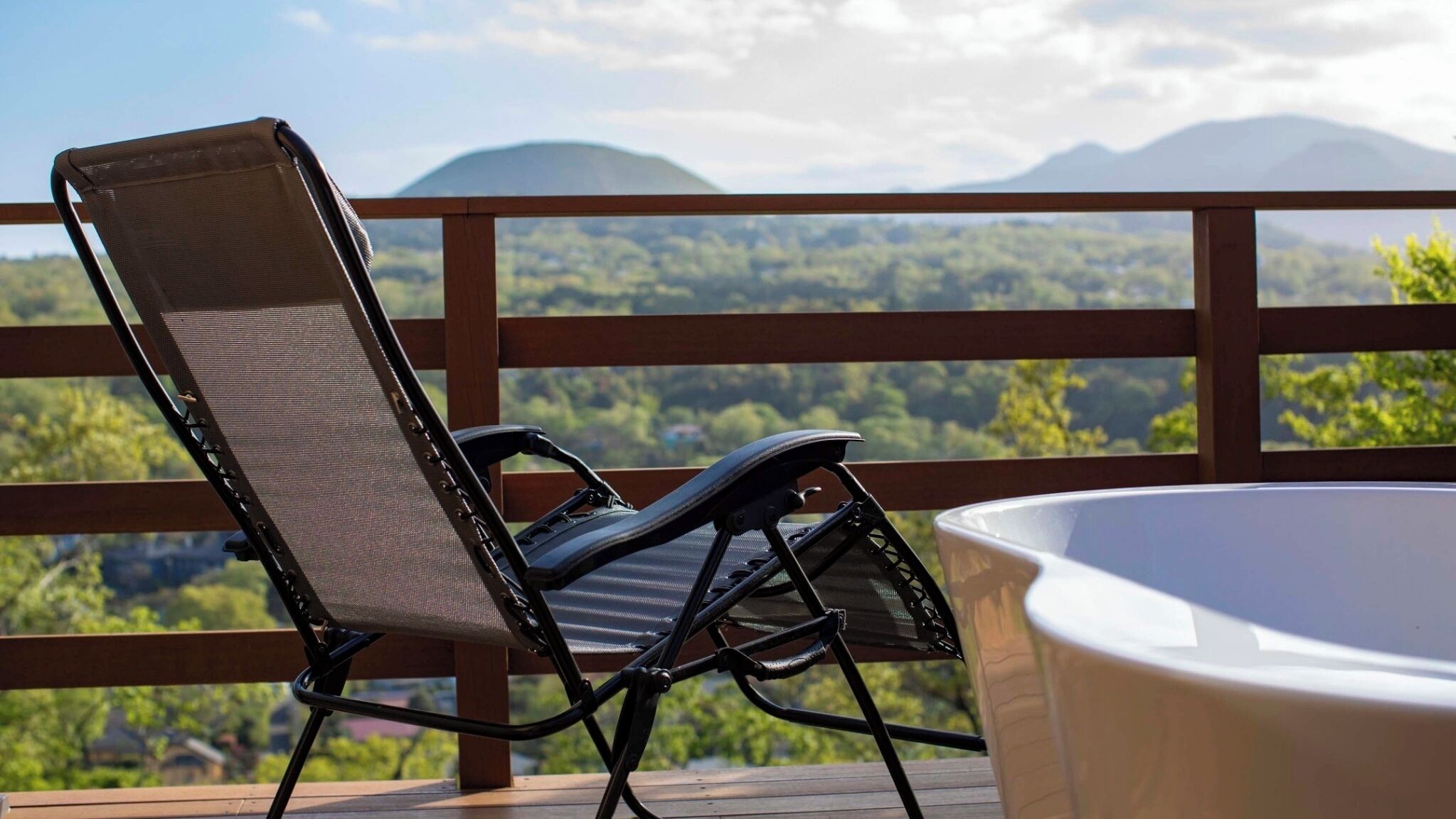 A deck with a chair and a hot tub overlooking a mountainous landscape.