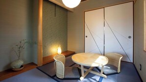 A traditional Japanese room with tatami flooring, a low table, two chairs, a lamp, and a shoji screen door.