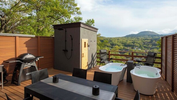 A deck with a hot tub, outdoor seating, and a barbecue grill.