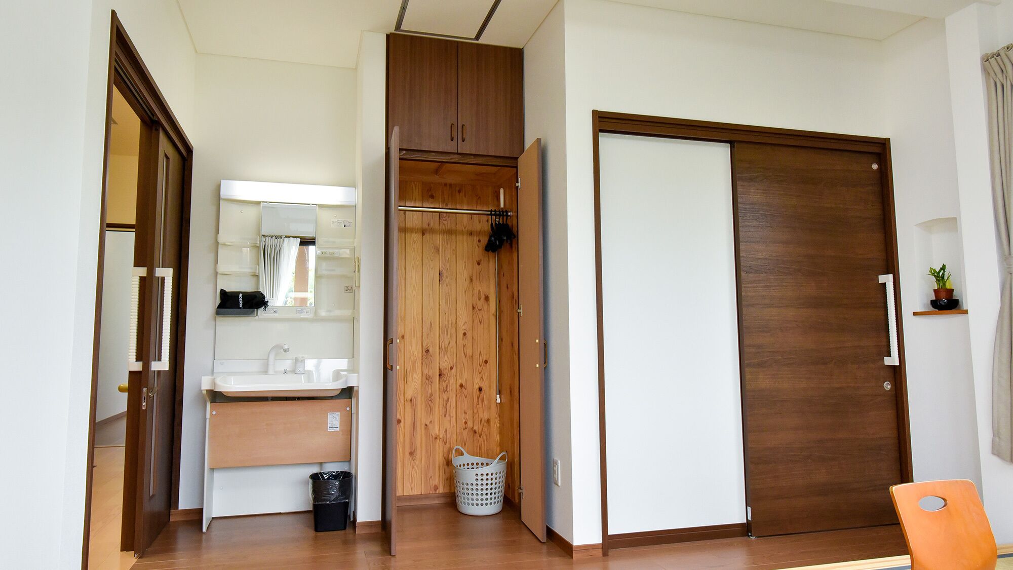 A compact room with a wooden wardrobe, a white sink, and a mirror.