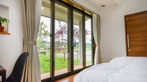 A bedroom with a large sliding glass door leading to a balcony, a bed with white bedding, and a wooden door. - Hotel Circle One (Sagara)