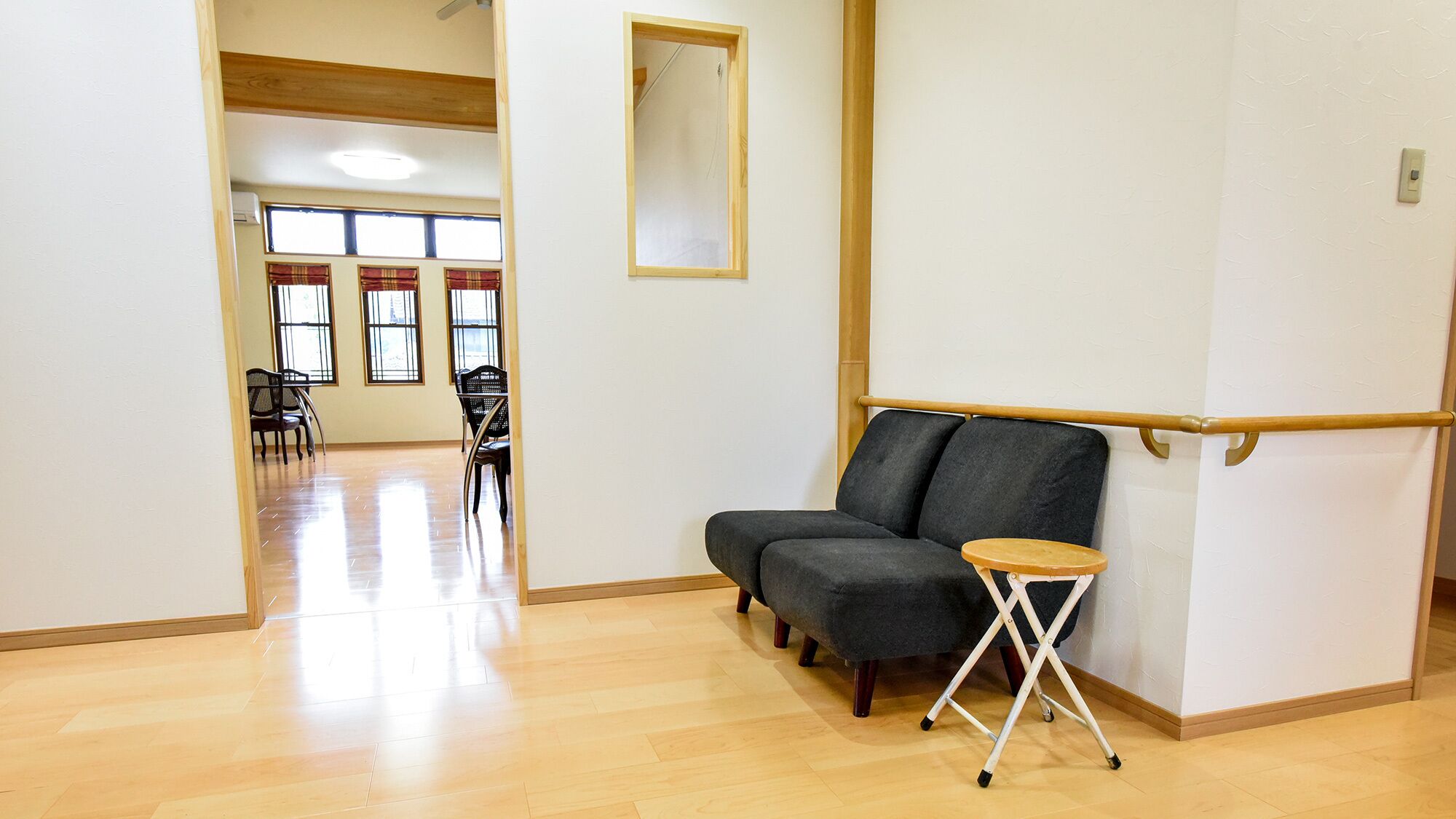 A room with a wooden floor, a grey sofa, a small wooden table, and a mirror on the wall.