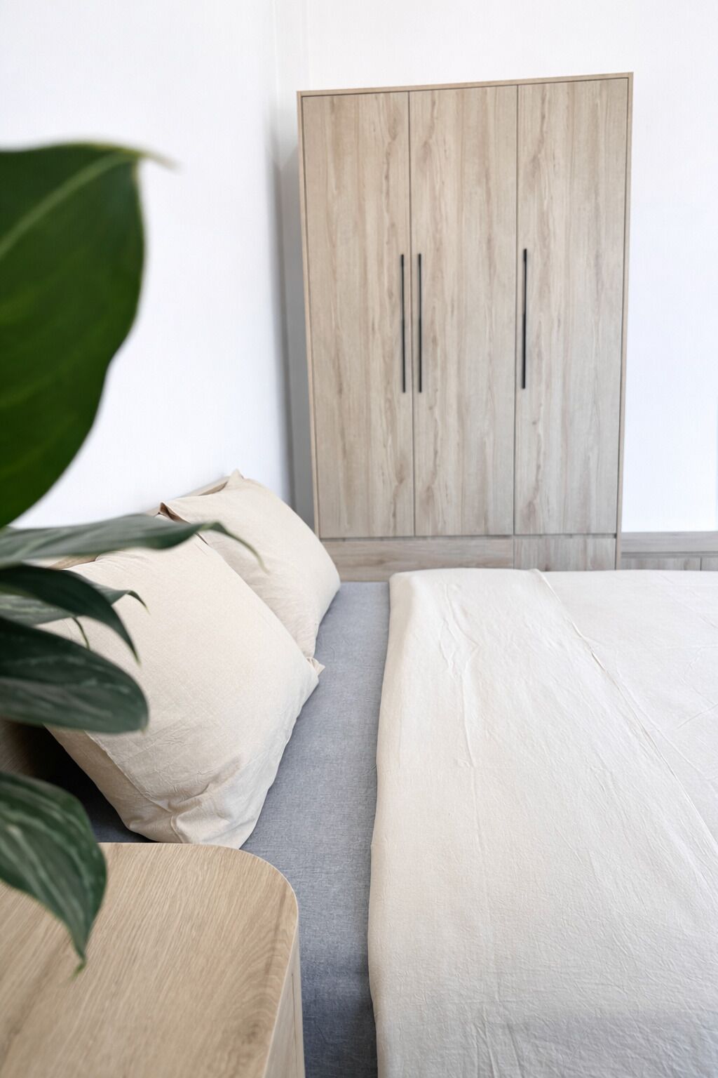 A bedroom with a bed, a grey sofa, and a wooden wardrobe.