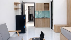 Una sala de estar moderna con un sofá gris, una mesa de centro redonda de madera con una computadora portátil, y una cocina al fondo.