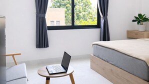 Un dormitorio moderno con una cama, un ordenador portátil sobre una mesita y una planta en maceta.