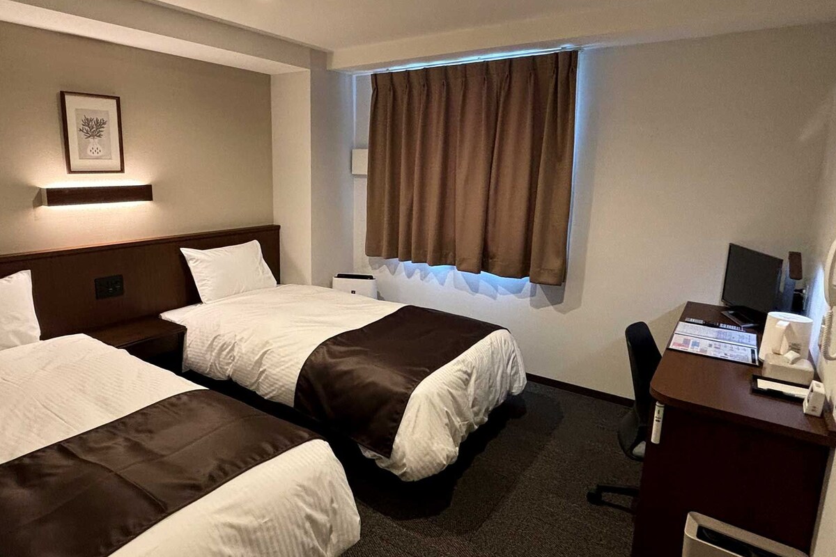 Ein Hotelzimmer mit zwei Betten, einem Schreibtisch mit Telefon und einem Vorhangfenster.