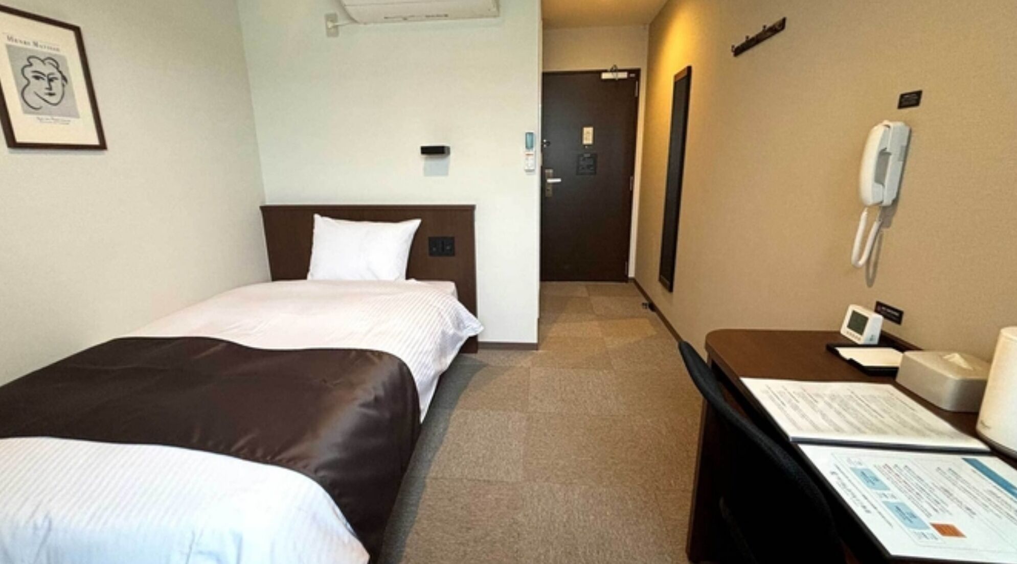 Une chambre d’hôtel avec deux lits, un bureau doté d’un téléphone et d’un appareil numérique, et un tableau encadré au mur.