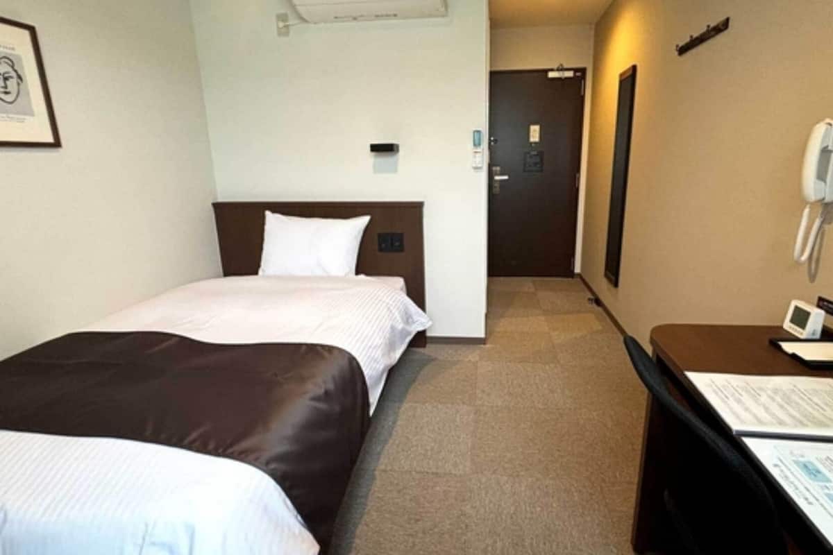 Une chambre d’hôtel avec deux lits, un bureau doté d’un téléphone et d’un appareil numérique, et un tableau encadré au mur.