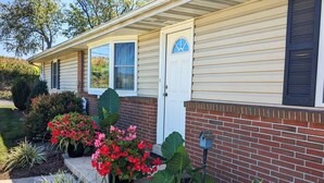 A single-story house with a brick facade and a white door. There are potted plants and a birdhouse on the front porch. - Hilltop Guesthouse - in Intercourse on Beacon Hill, 4-Bedroom House (Ronks)