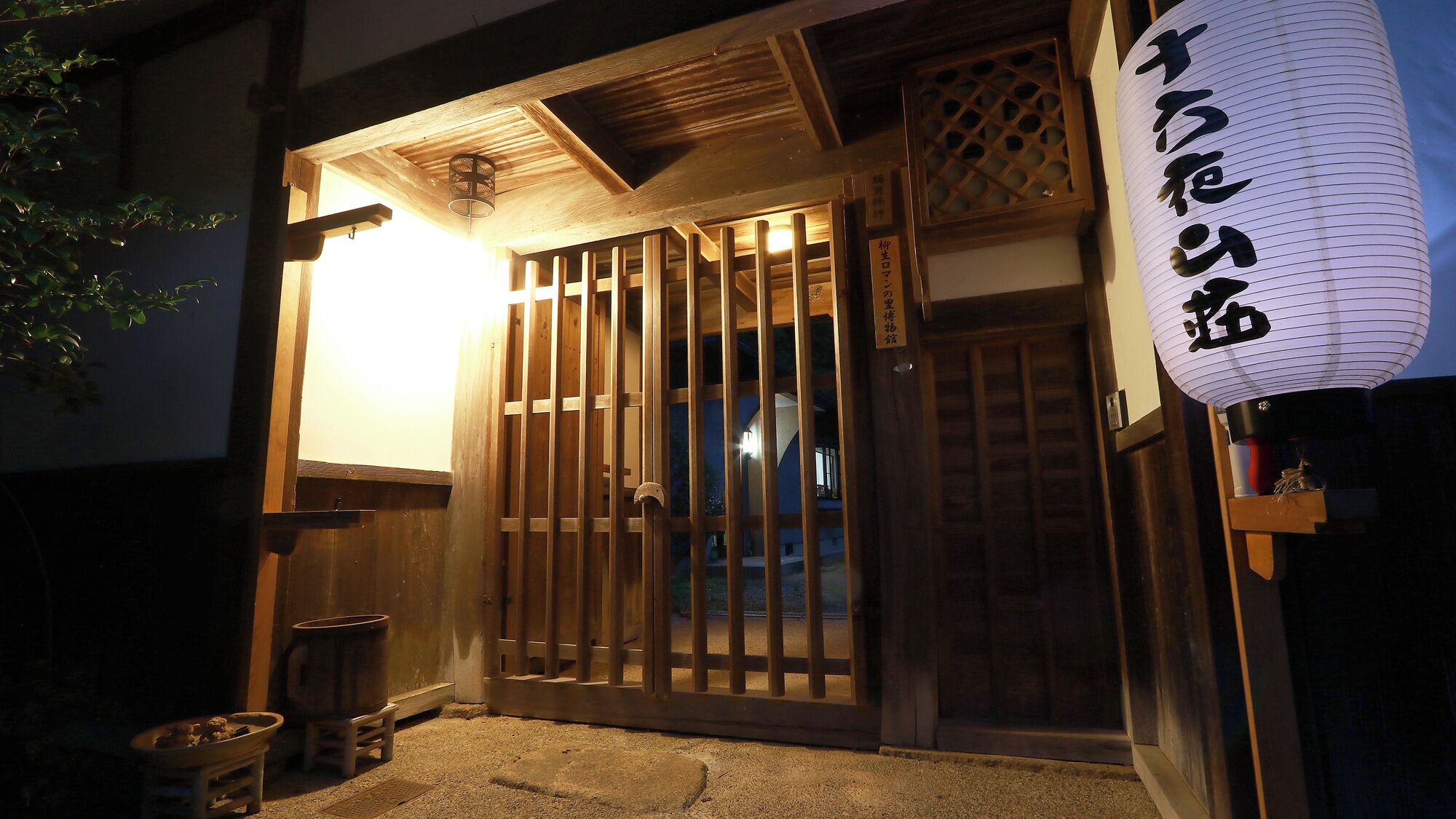 A traditional Japanese building with a wooden gate, a lantern, and a sign with Japanese characters.