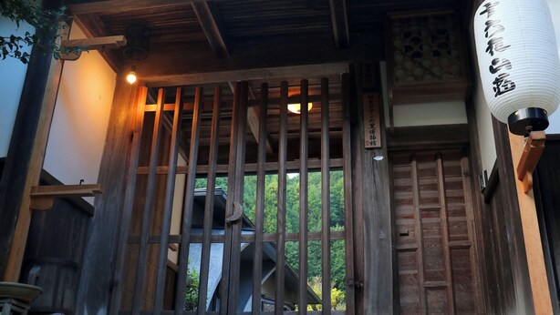 Une porte traditionnelle en bois, avec des barreaux verticaux, une lanterne et une enseigne portant des caractères japonais.