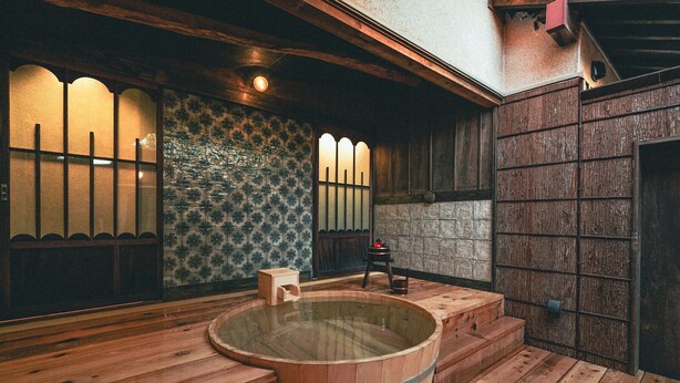 A traditional Japanese onsen with a wooden hot tub, wooden steps, and a tiled wall with a geometric pattern. - The Timeless Hotel Loof Yunoie (Yachiyo)