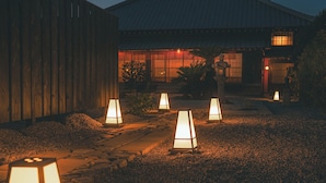 A traditional Japanese house with a tiled roof, surrounded by gravel and illuminated by several lanterns. - The Timeless Hotel Loof Yunoie (Yachiyo)