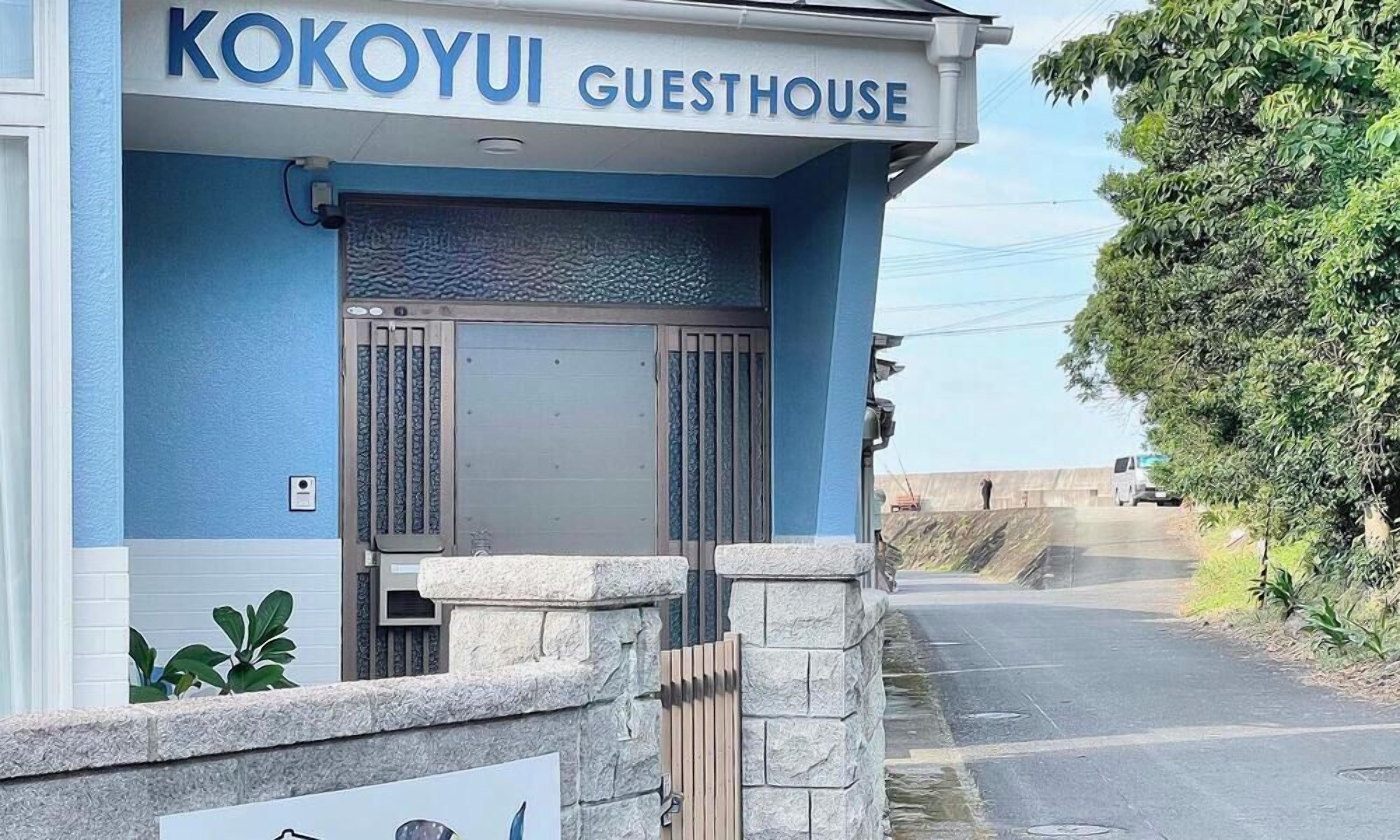 A guesthouse named 'Kokoyui' with a blue exterior, a gated entrance, and a stone wall in front.