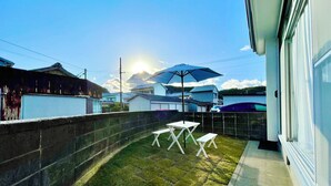 A residential backyard with a white table and chairs, a blue umbrella, and a brick wall.