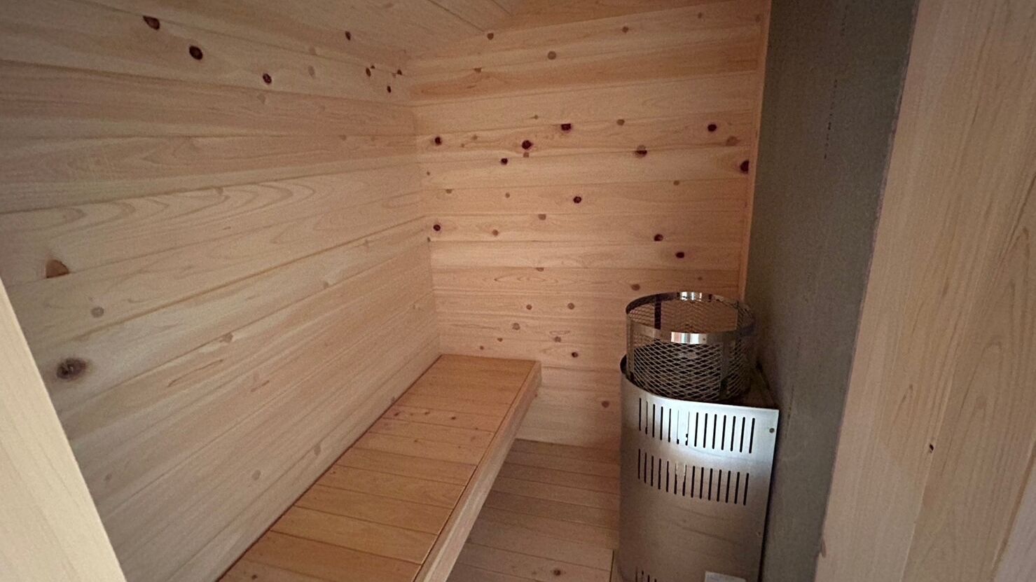 A wooden sauna room with a bench and a metal heater.