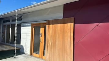 A modern building with a red wall, a wooden door, and a chain-link fence.