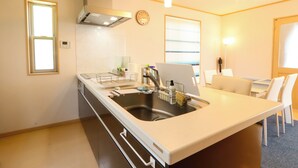 A modern kitchen with a built-in sink, a stove, and a dining area with a table and chairs. - K-style Resort (Yugawara)