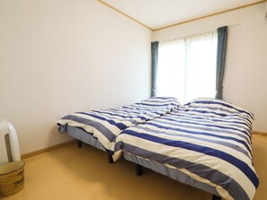A room with two beds, a window with curtains, a trash bin, and a wall-mounted air conditioning unit. - K-style Resort (Yugawara)