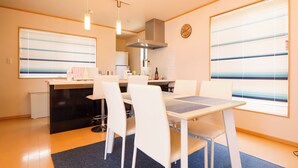 A modern kitchen with a dining area, featuring a clock, a stove, and a window with blinds. - K-style Resort (Yugawara)