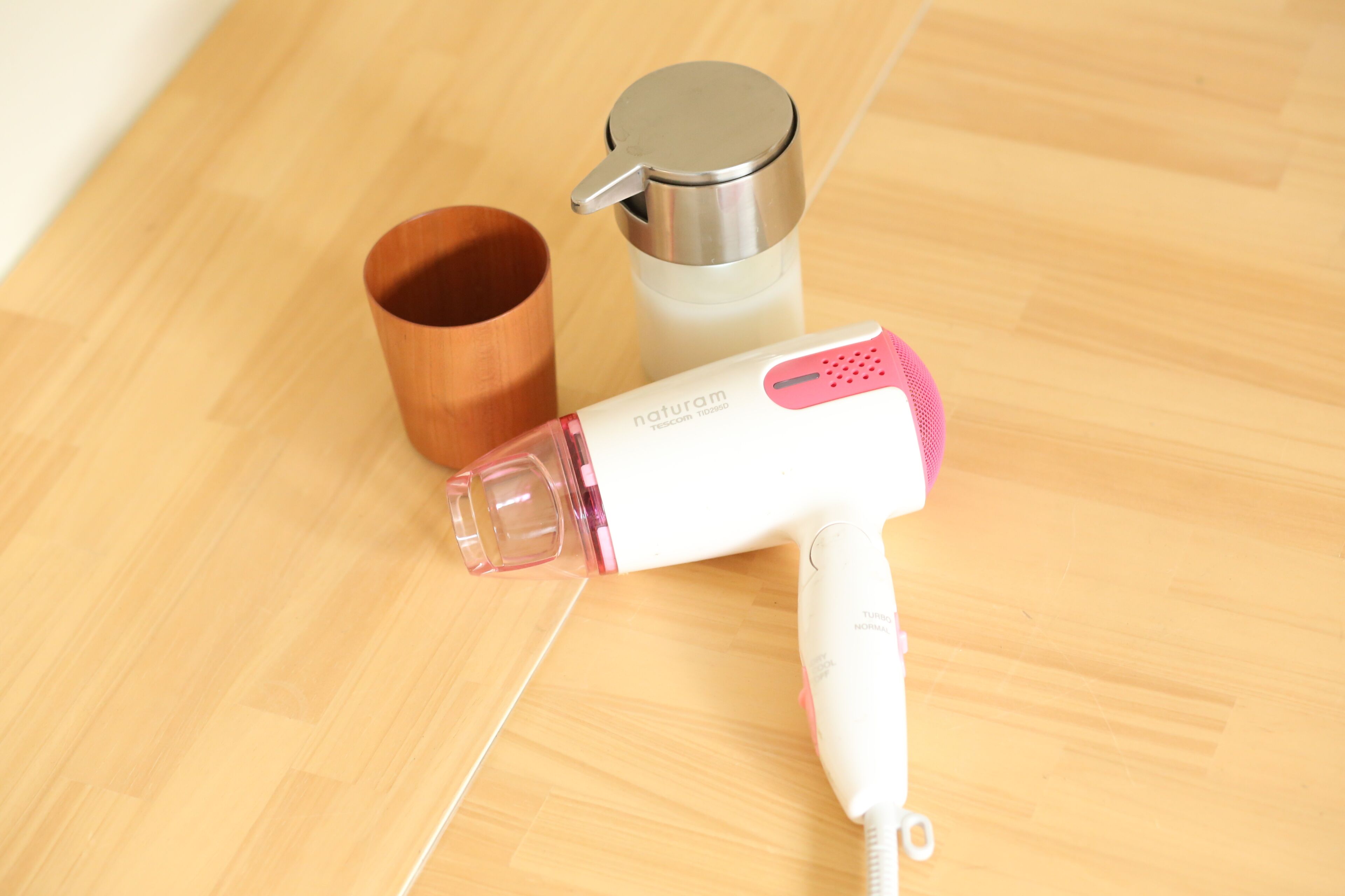 A hair dryer, a thermos, and a wooden cup on a wooden floor.