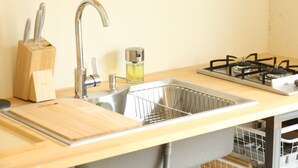 Una cocina con pileta, grifo, tabla de cortar de madera, bloque de cuchillos y cocina a gas.