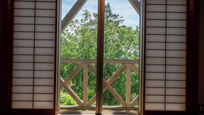 Blick durch ein schmales Holzfenster mit Gittermuster, das auf einen Balkon mit Holzbalkon führt.