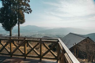 Una pasarela de madera con barandilla metálica da vista a un valle y montañas distantes.