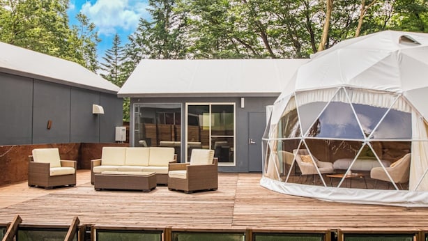 A modern outdoor living area with a wooden deck, a white tent-like structure, and a grey building with large windows. - Glamping Resort ITU (Nasu)