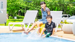 Two children playing in a pool with lounge chairs and a car in the background.