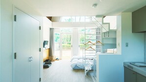 A compact, modern bedroom with a bunk bed, a small seating area with a basket, and a view of greenery through large windows.